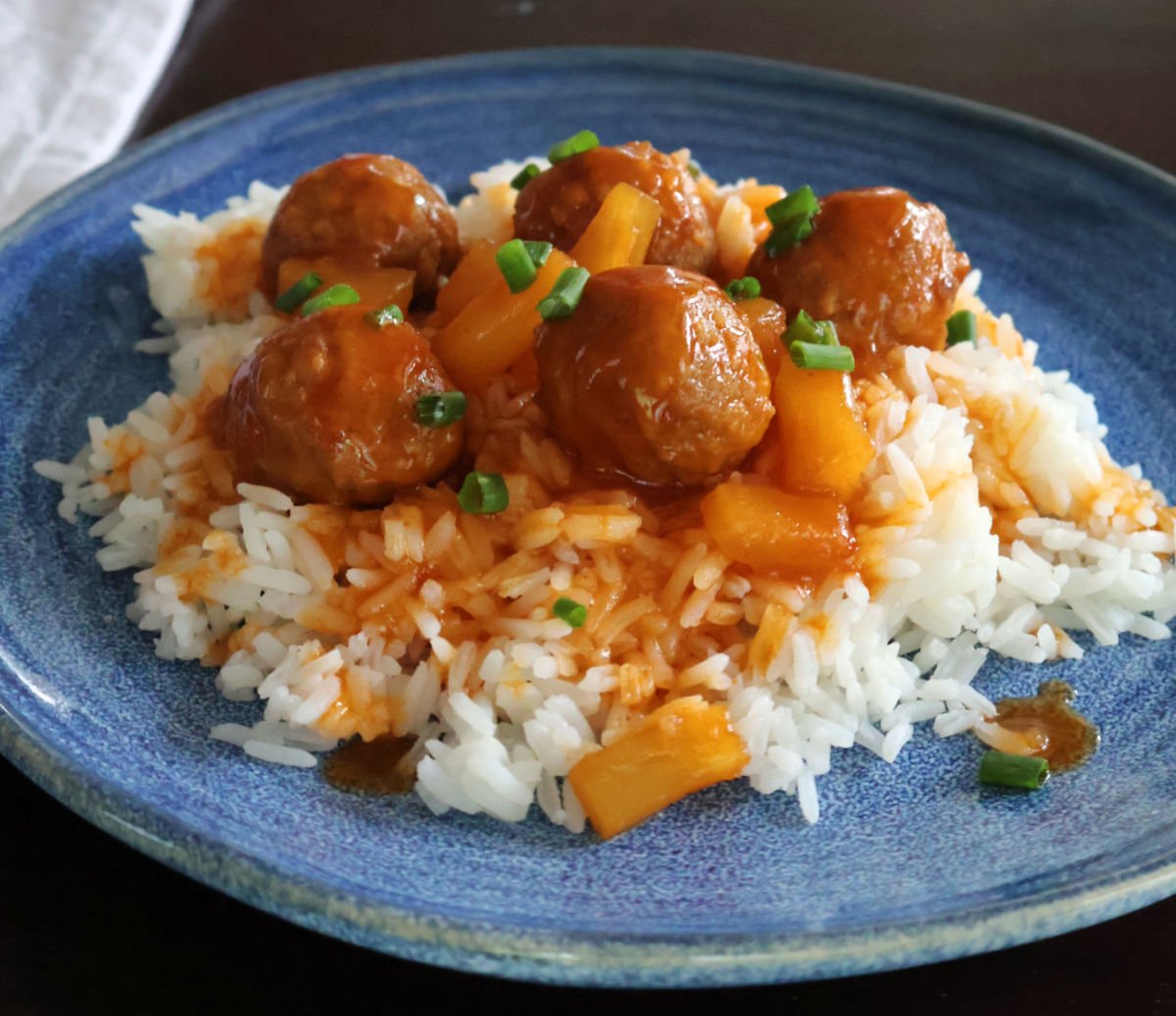 Meatballs on rice with a  sweet and sour sauce drizzled on top of the meatballs and rice. Pineapple tidbits are visible in the sauce. 