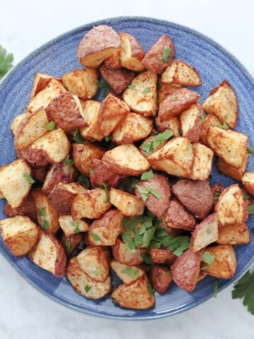 Air fryer roasted red potatoes garnished with parsley swerved on a blue plate.