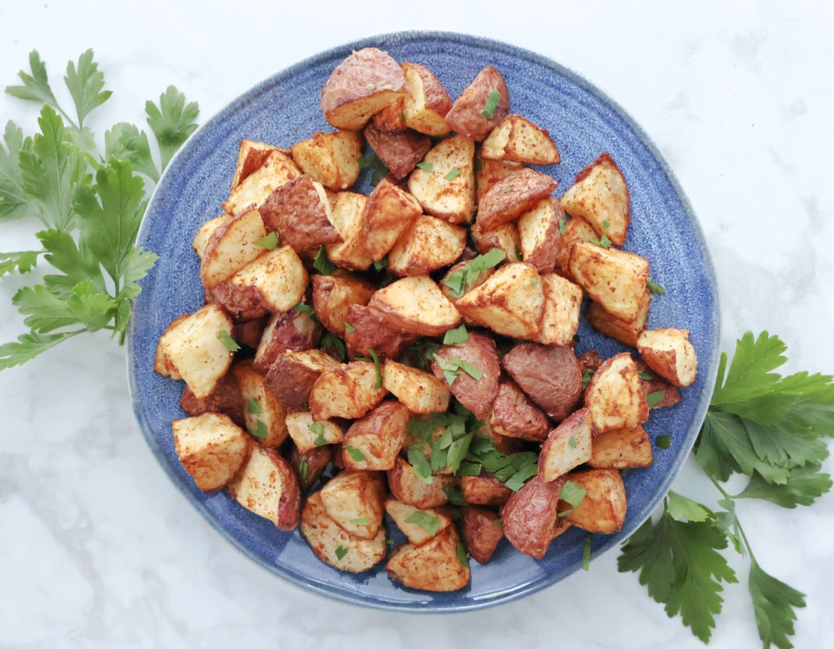 Air fryer roasted red potatoes garnished with parsley swerved on a blue plate.