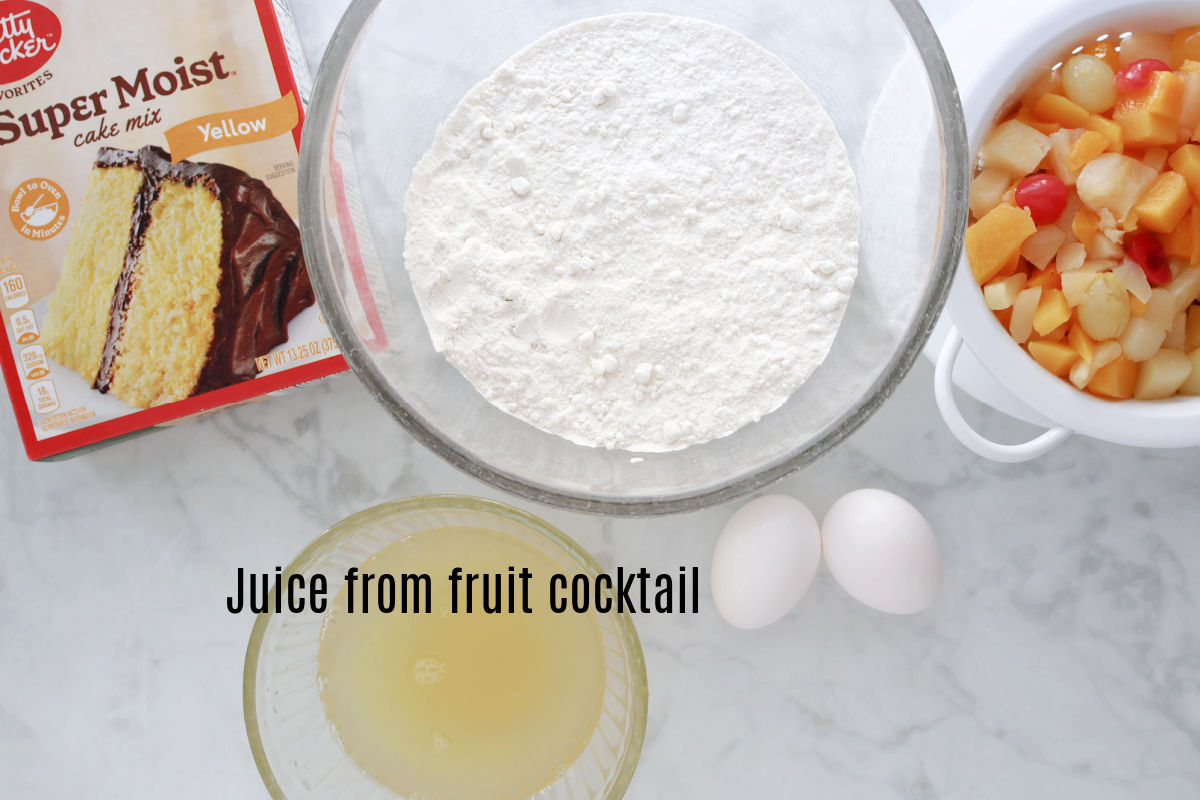 Fruit cocktail upside down mix ready to be put together.  A bowl of cake mix, a small bowl of juide from the fruit cocktail cans, two eggs and a small colander with the fruit cocktail.