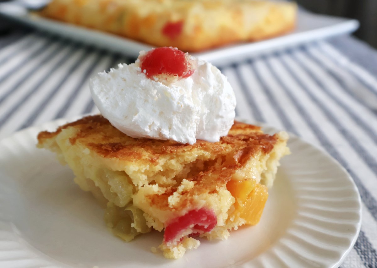 Fruit Cocktail cake served with the fruit on the bottom and golden crust on top. Topped with whipped cream and a red cherry.