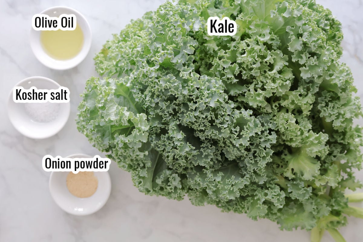 A large pile of fresh kale, withe small bowls of olive oil, kosher salt and onion power beside it.