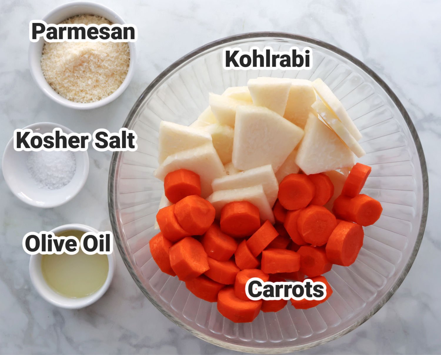 Kohlrabi and carrots cut up shown in a glass bowl.  Kosher salt, Olive oil and optional parmesan cheese shown in small containers on left of large bowl.