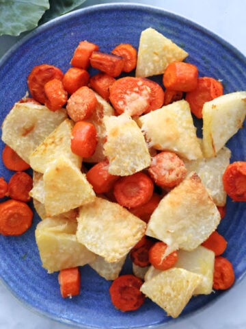 cut up kohlrabi and carrots, roasted in the oven with melted slightly golden parmesan cheese on top. Shown on a blue plate.