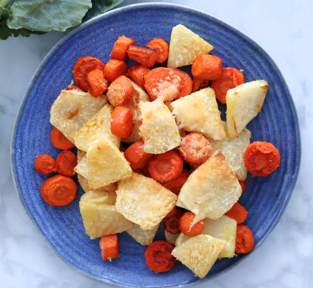 cut up kohlrabi and carrots, roasted in the oven with melted slightly golden parmesan cheese on top. Shown on a blue plate.