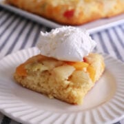 Fruit cocktail cake flipped so that the fruit is on top. Served on a white plate with some whipped topping.