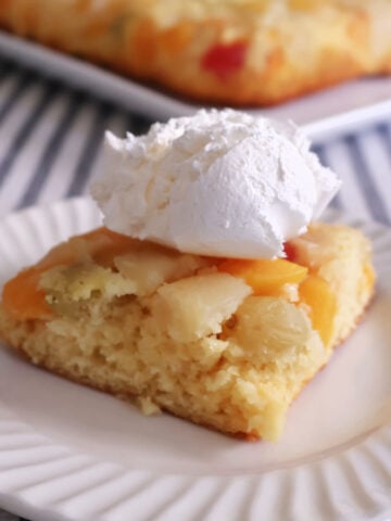 Fruit cocktail cake flipped so that the fruit is on top. Served on a white plate with some whipped topping.