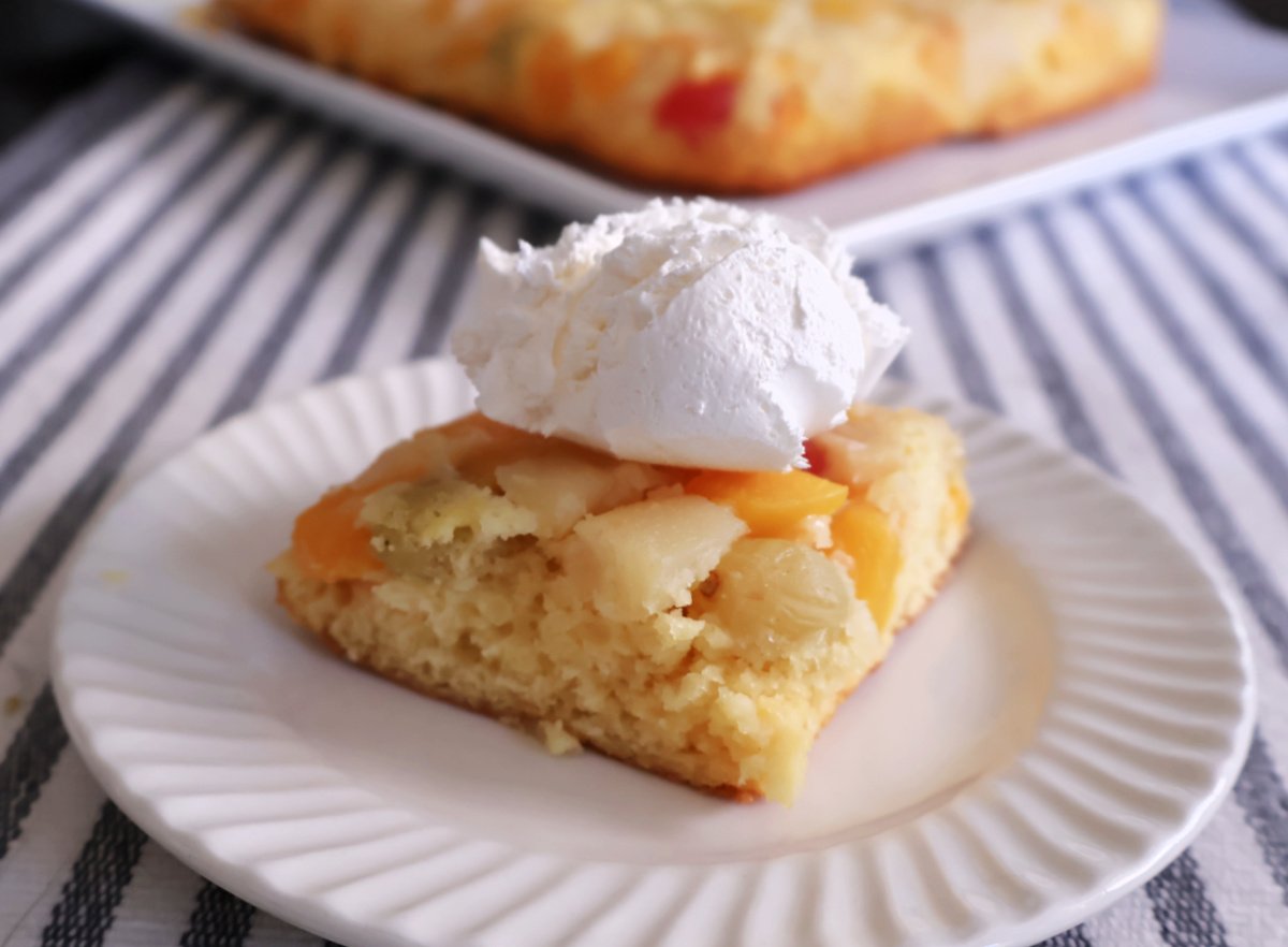 Fruit cocktail cake flipped so that the fruit is on top. Served on a white plate with some whipped topping.