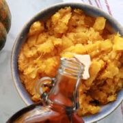 A bowl of air fryer acorn squash with a pat of butter and some maple syrup being poured on it.