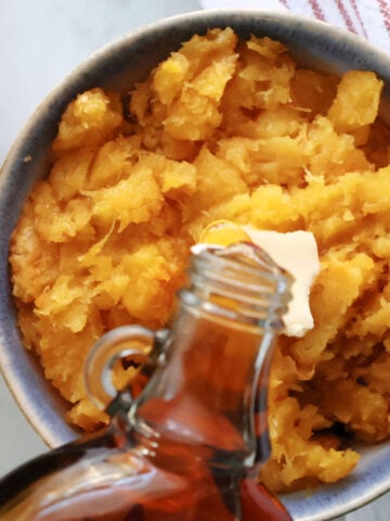 A bowl of air fryer acorn squash with a pat of butter and some maple syrup being poured on it.