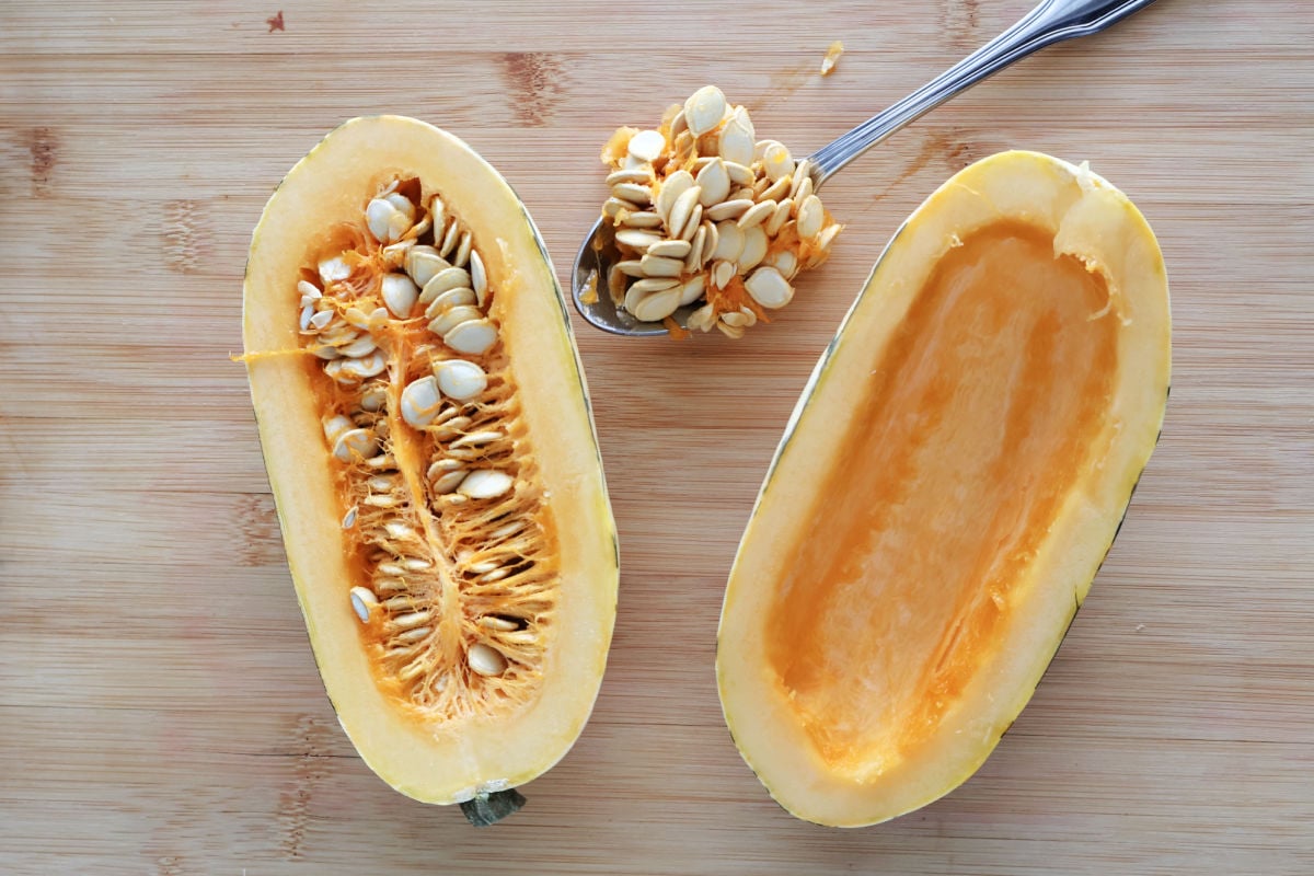 delicata squash cut in half. One side still has the seeds in it, the other side has the seeds scooped out on a spoon.