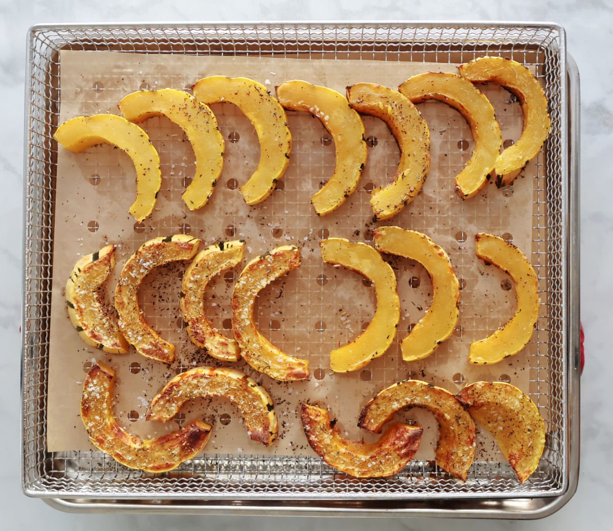 sliced delicata squash being flipped on a tray to finish cooking in the air fryer.