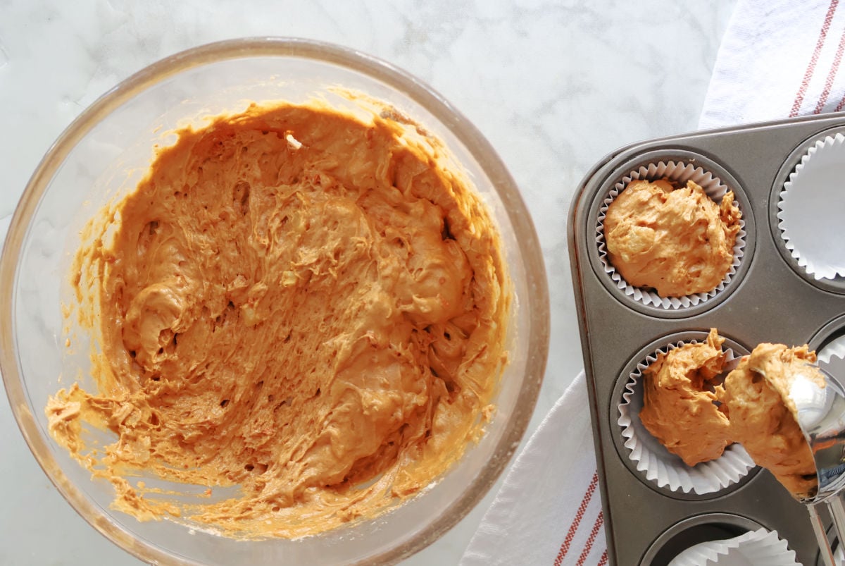 Carrot muffin batter being scooped into muffin tin.