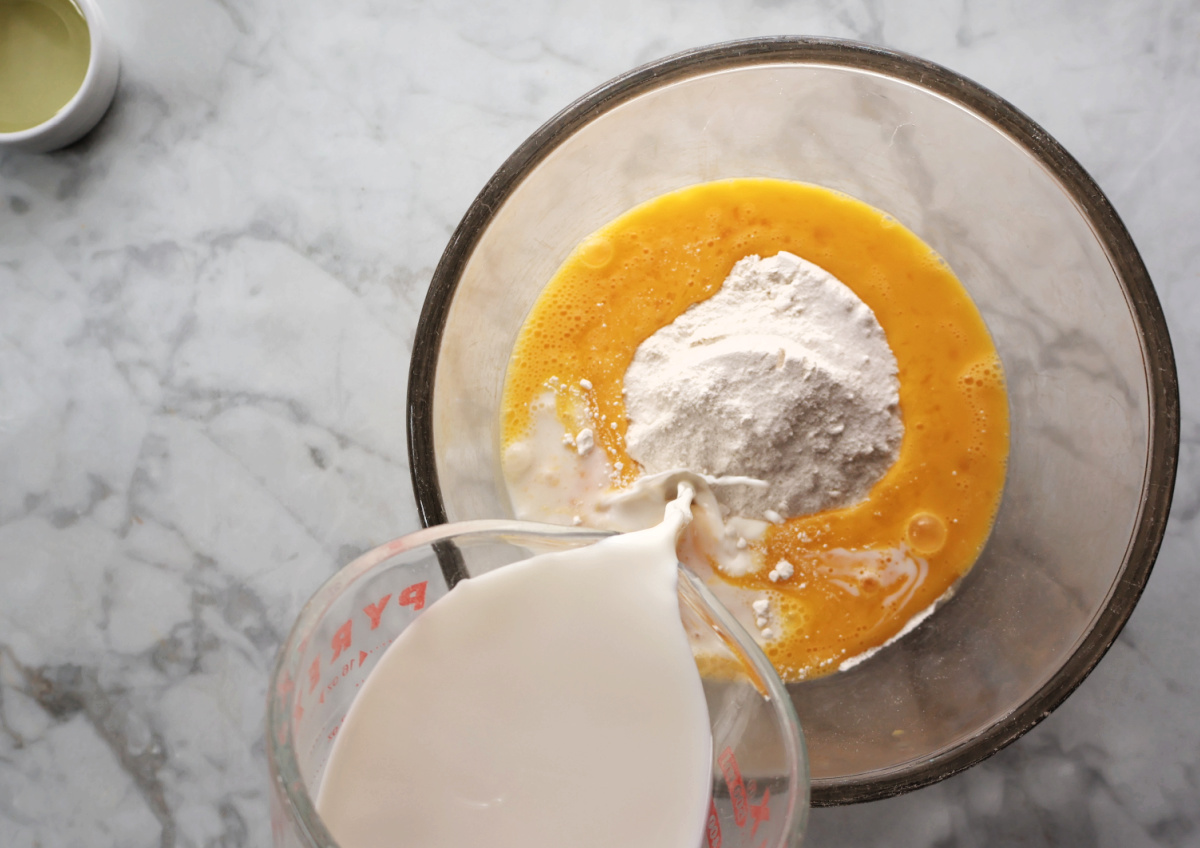 Pouring milk into bowl with whisked eggs and flour to make yorkshire pudding.