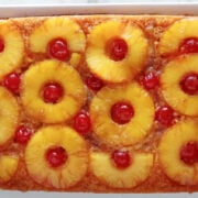 Colorful pineapple upside down cake with pineapple rings with a maraschino cherry inside each ring. You can see the caramel topping running down the side of the cake.