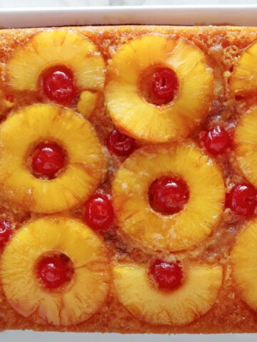 Colorful pineapple upside down cake with pineapple rings with a maraschino cherry inside each ring. You can see the caramel topping running down the side of the cake.