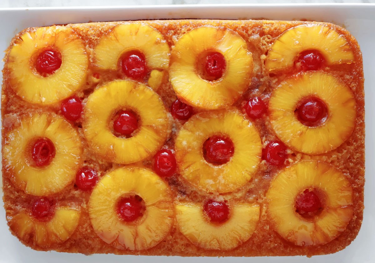 Colorful pineapple upside down cake with pineapple rings with a maraschino cherry inside each ring. You can see the caramel topping running down the side of the cake.