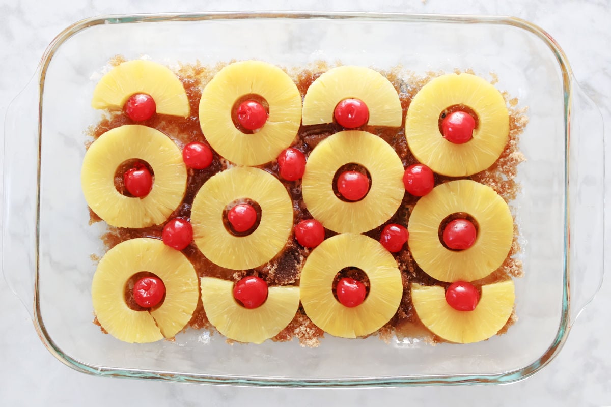 pineapple rings with maraschino cherries in the centers on top of a layer of melted butter and brown sugar.