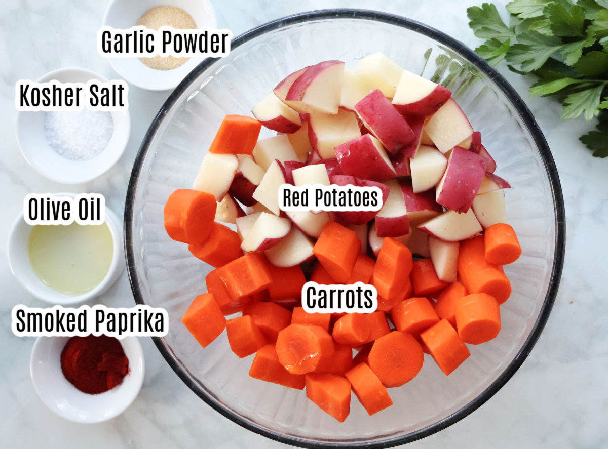 cut up red potatoes and carrots in a glass bowl. Small containers beside the  big bowl hold garlic powder, Kosher salt, Olive oil and smoked paprika.