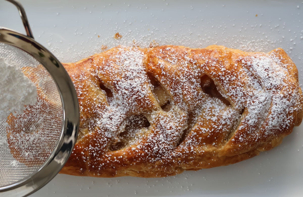 Dusting top of apple strudel with icing sugar.