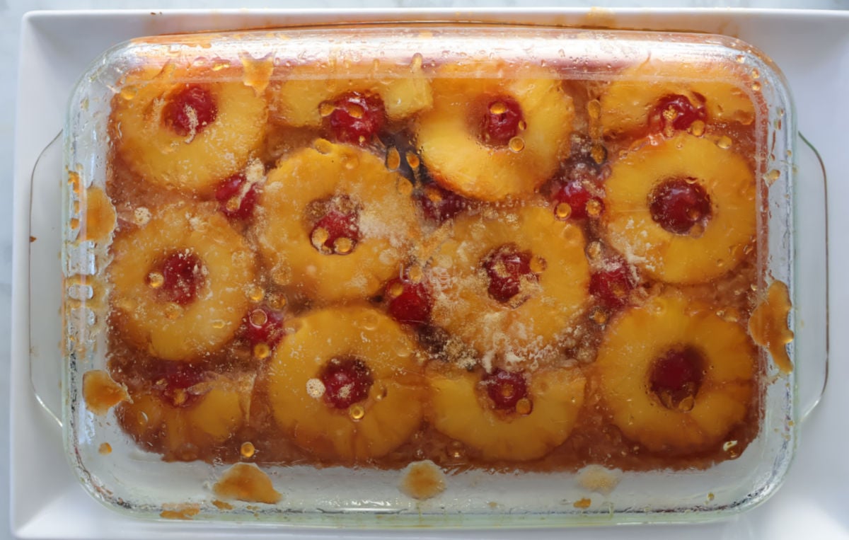 Flipping the clear glass baking dish showing the finished pineapple upside down cake through the pan.