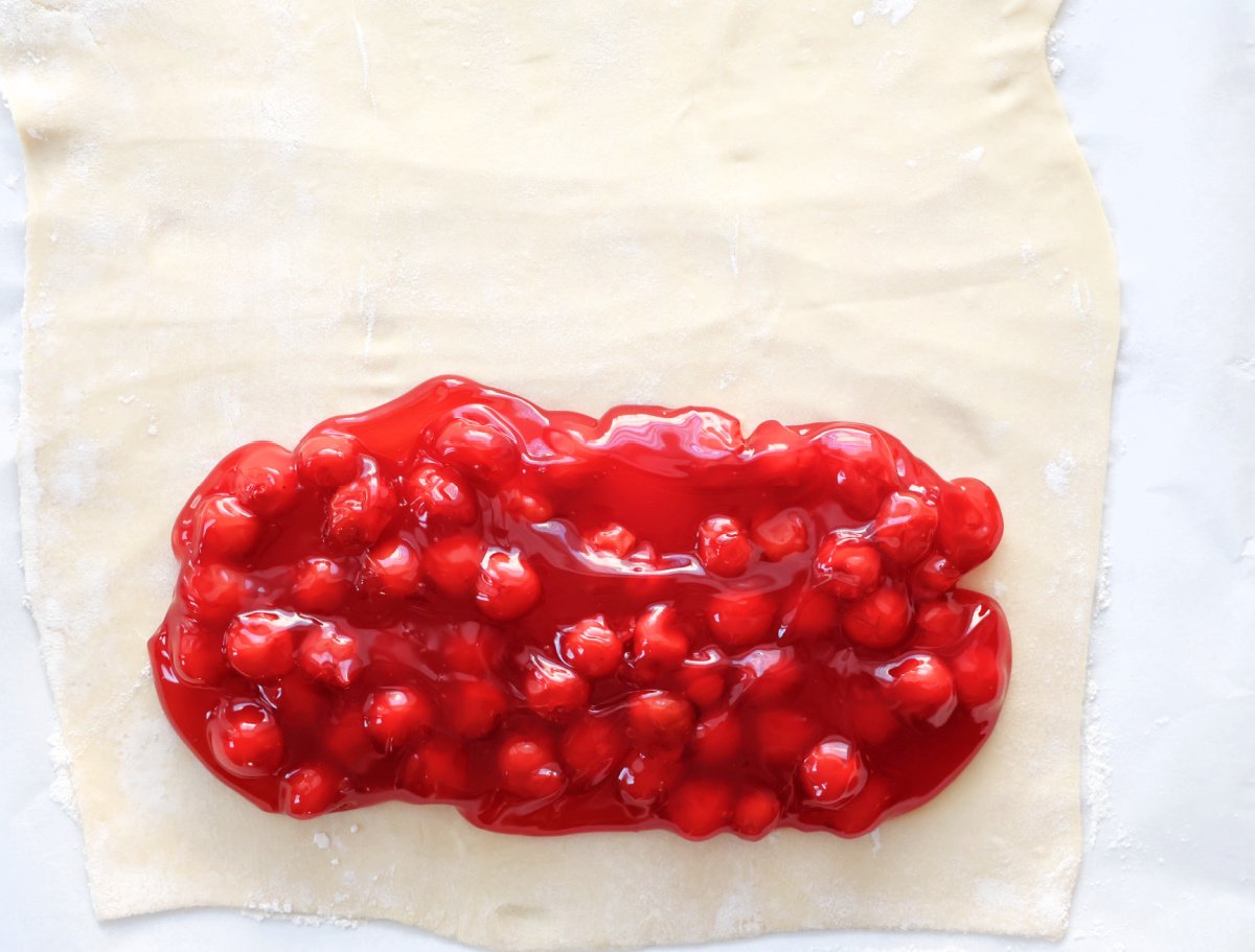 Cherry pie filling on bottom section of rolled out puff pastry. Ready to be wrapped to make cherry strudel.