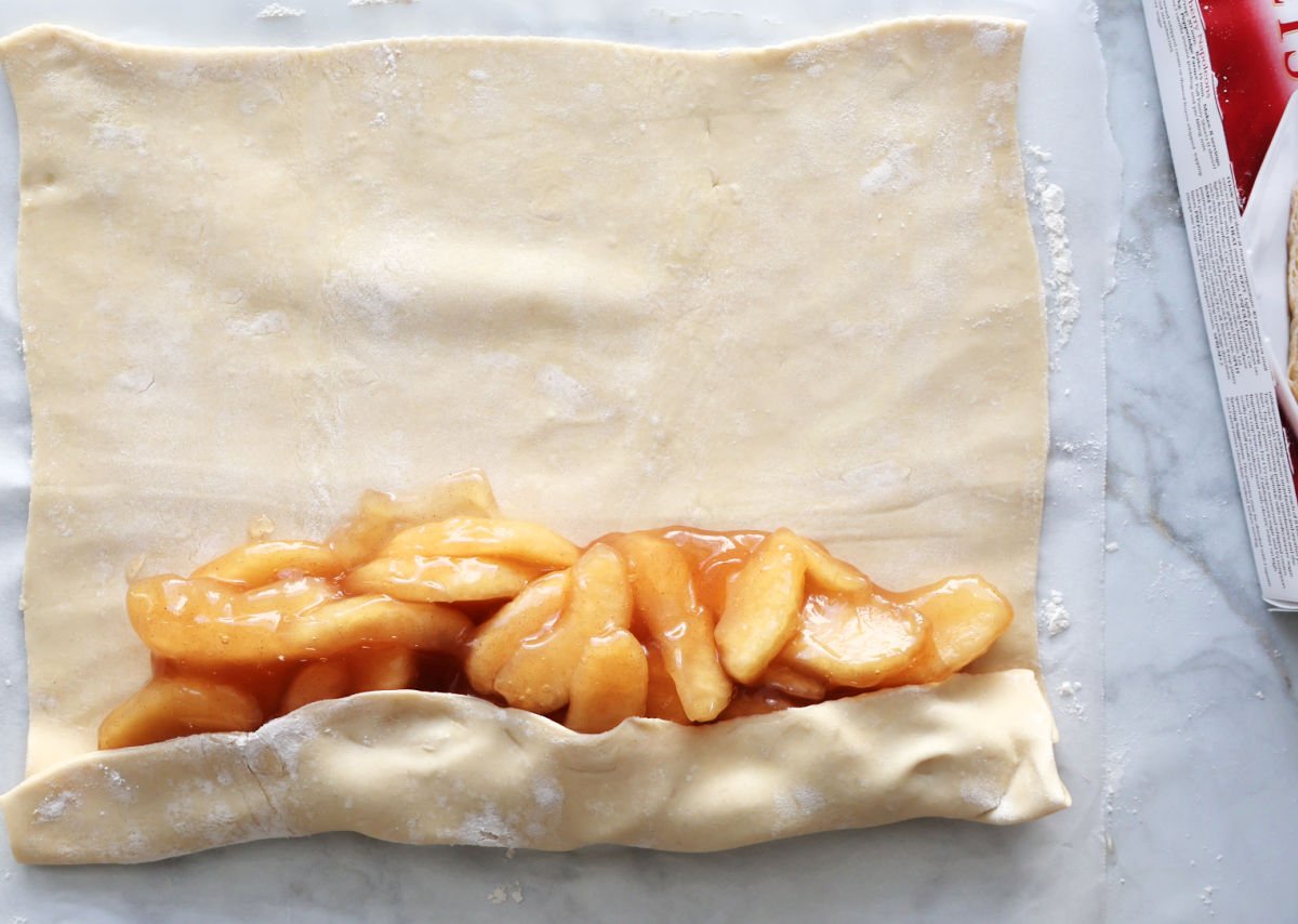 Rolling puff pastry around the apple pie filling.