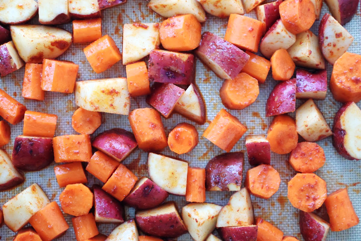 seasoned red potatoes and carrots with smoked paprika on a silicone mat ready for the pan to go into the oven.