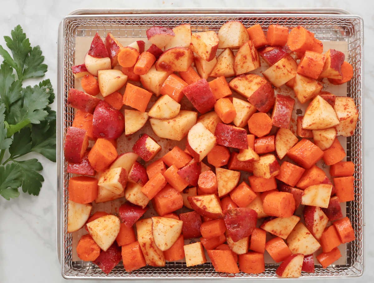 seasoned red potatoes and carrots in a single layer in an air fryer basket