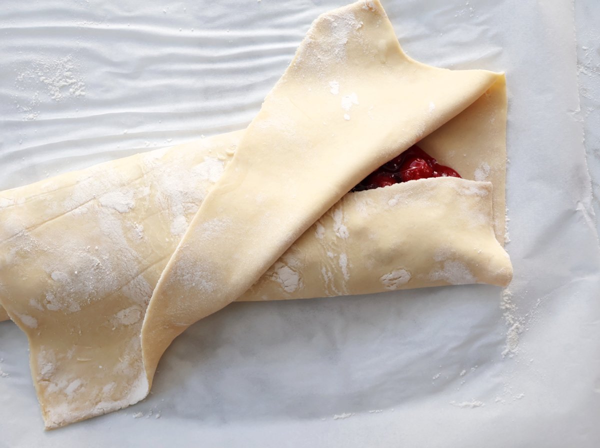 puff pastry being rolled around cherry pie filling.