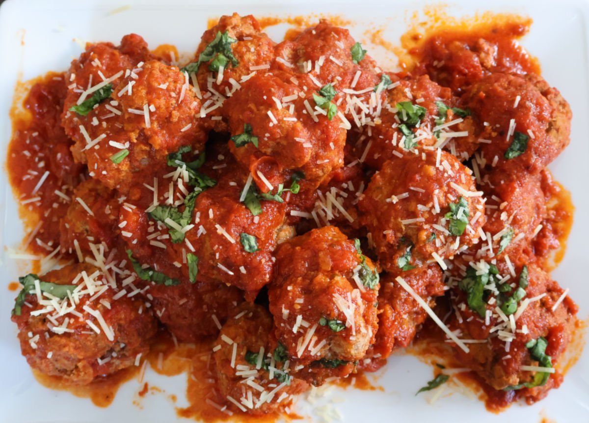 A serving plate full of ricotta meatballs with a sprinkling of parasan cheese and slivered basil on top.