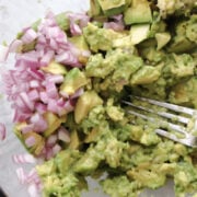 avocado being mashed and red onions added to recipe for fresh guacamole,