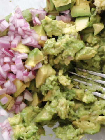 avocado being mashed and red onions added to recipe for fresh guacamole,