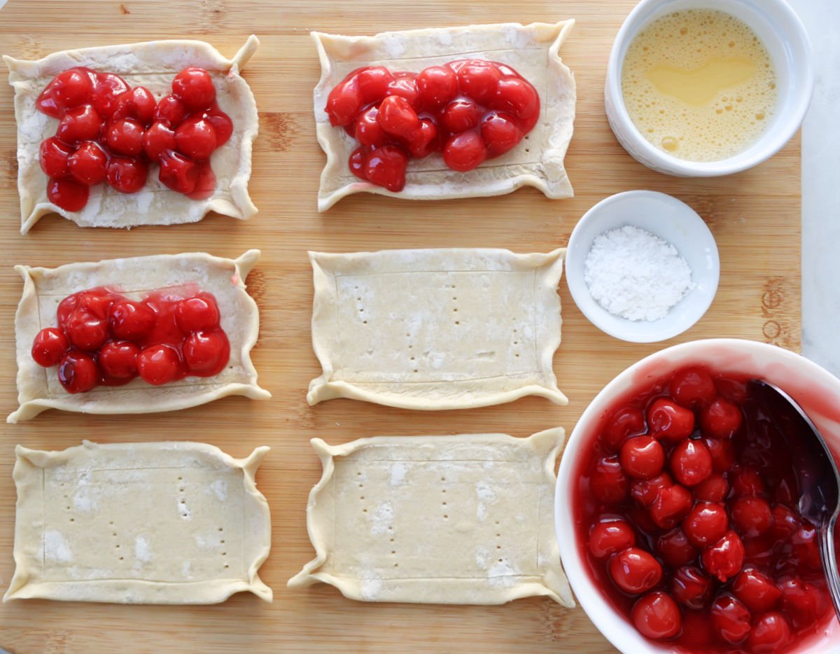 assembling cherry danish with cherry pie filling placed on some of the cut out puff pastry portions.