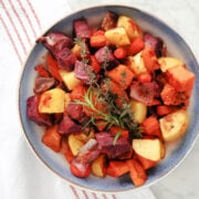 Roasted sweet potatoes in a serving bowl. Includes roasted potatoes, sweet potatoes, purple sweet potatoes, carrots and red onions. Seasoned then garnished with a sprig of rosemary and some thyme.