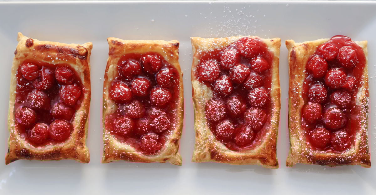 4 cherry danishes made with puff pastry and cherry pie filling on a white tray with a dusting of powdered sugar