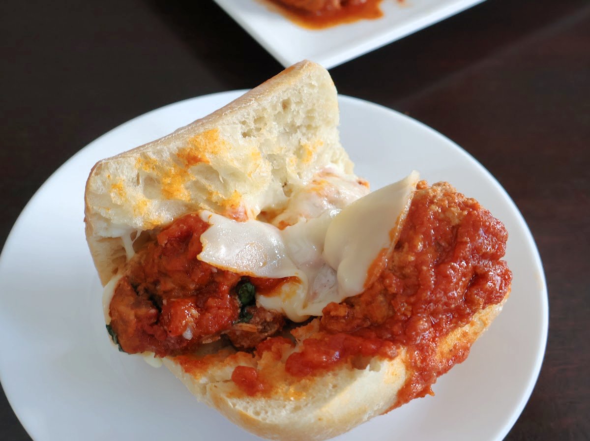 sub meatball with melted cheese and marinara sauce on a white plate.