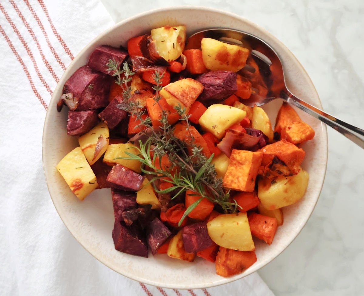 cut up roasted root vegetables including yellow potatoes, orange sweet potaotes, purple sweet potatoes and red onion.  Also includes thyme leaves and rosemary. 