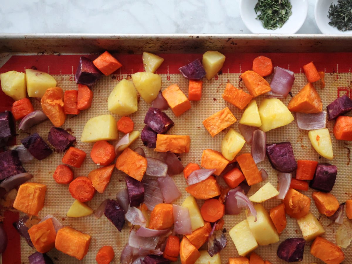 Roasted root vegetables on a sheet pan.  Includes potatoes, sweet potatoes, carrots, purple sweet potatoes and red onions.