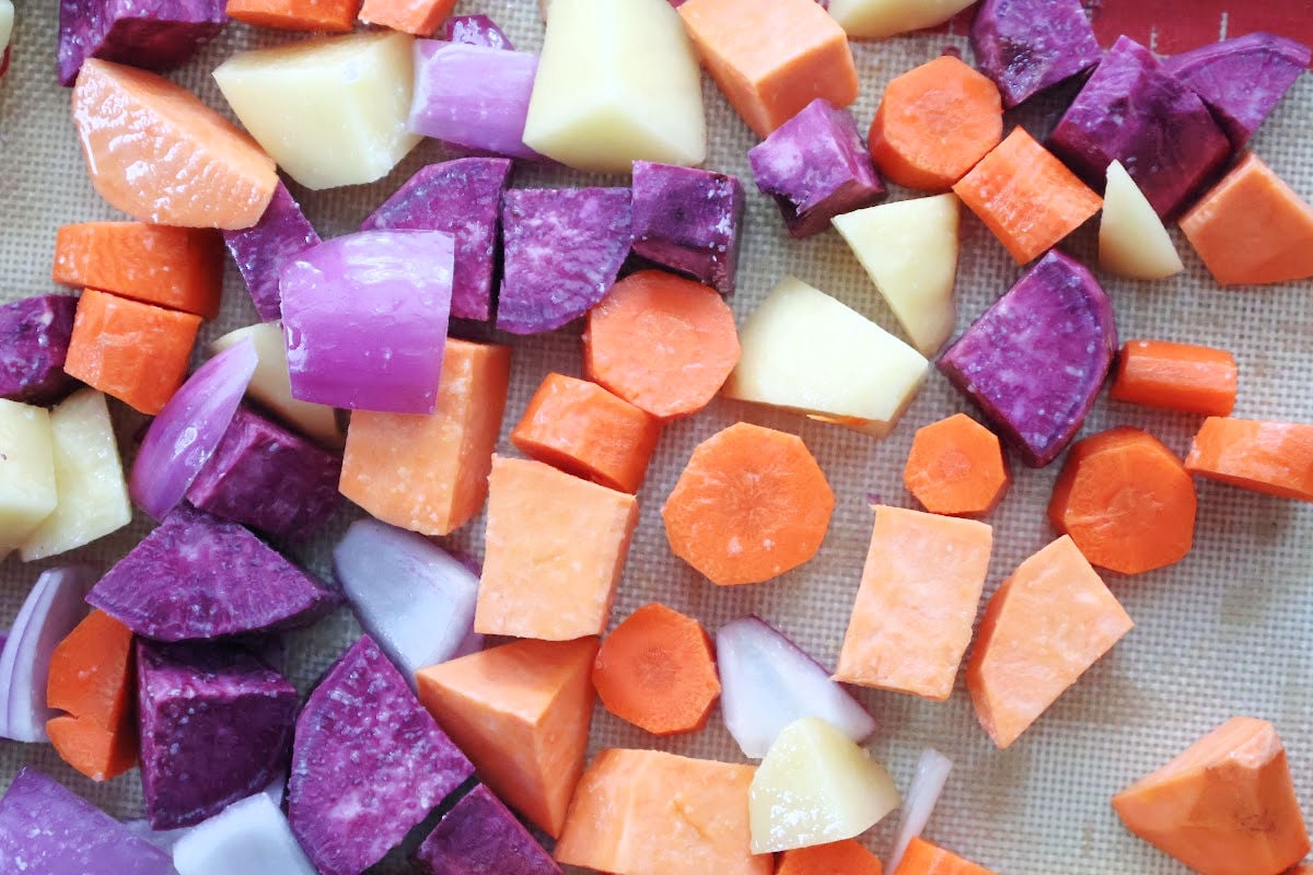 colorful root vegetables on a sheetpan.  Vegetables include potatoes, sweet potatoes, purple sweet potatoes, carrots and red onions