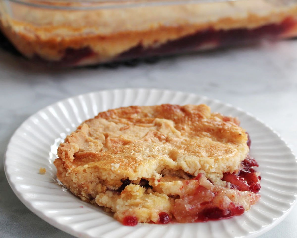 apple cranberry dump cake served on a white plate with the baking dish behind the plate.