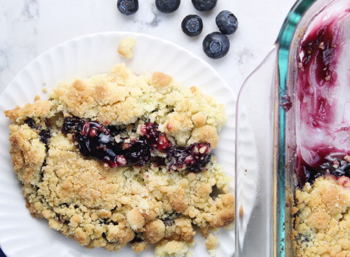 Blueberry cobbler served on a white plate.  The cobbler is sitting beside the baking pan that is already half empty because people enjoy it so much!
