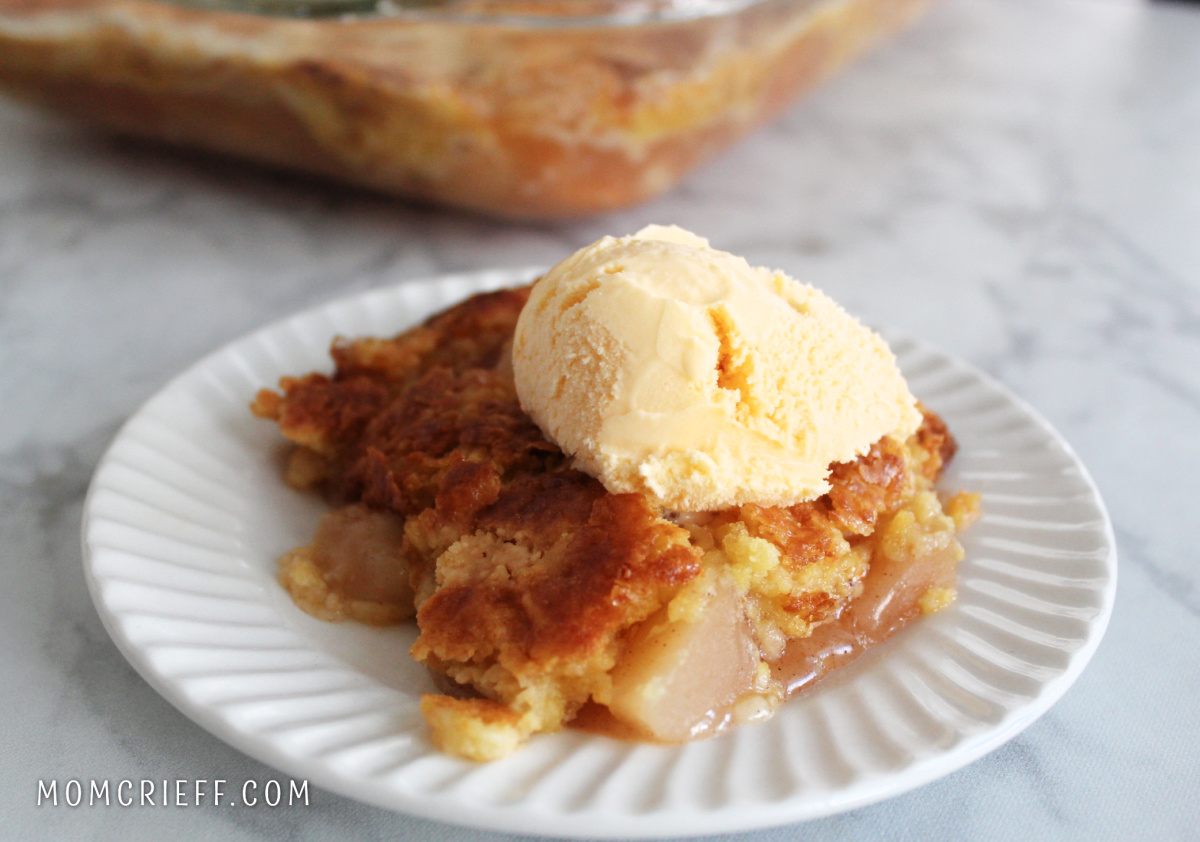 apple dump cake on a white plae with a scoop of ice cream on top. The apples look delicious and tender and the crust is a pretty golden brown,