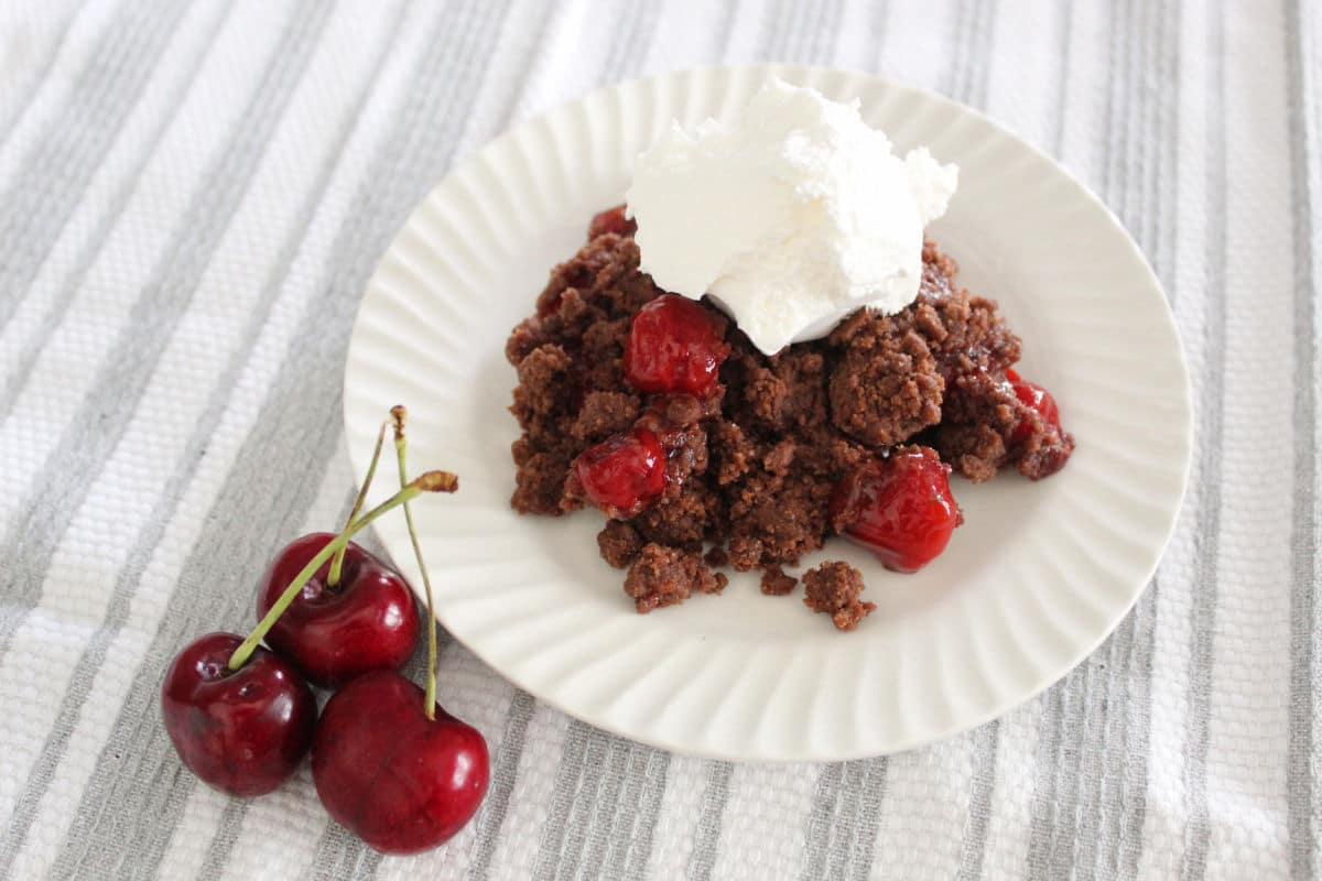 chocolate cherry dump cake serving topped with some ice cream.  Fresh cherries are visible beside the plate.