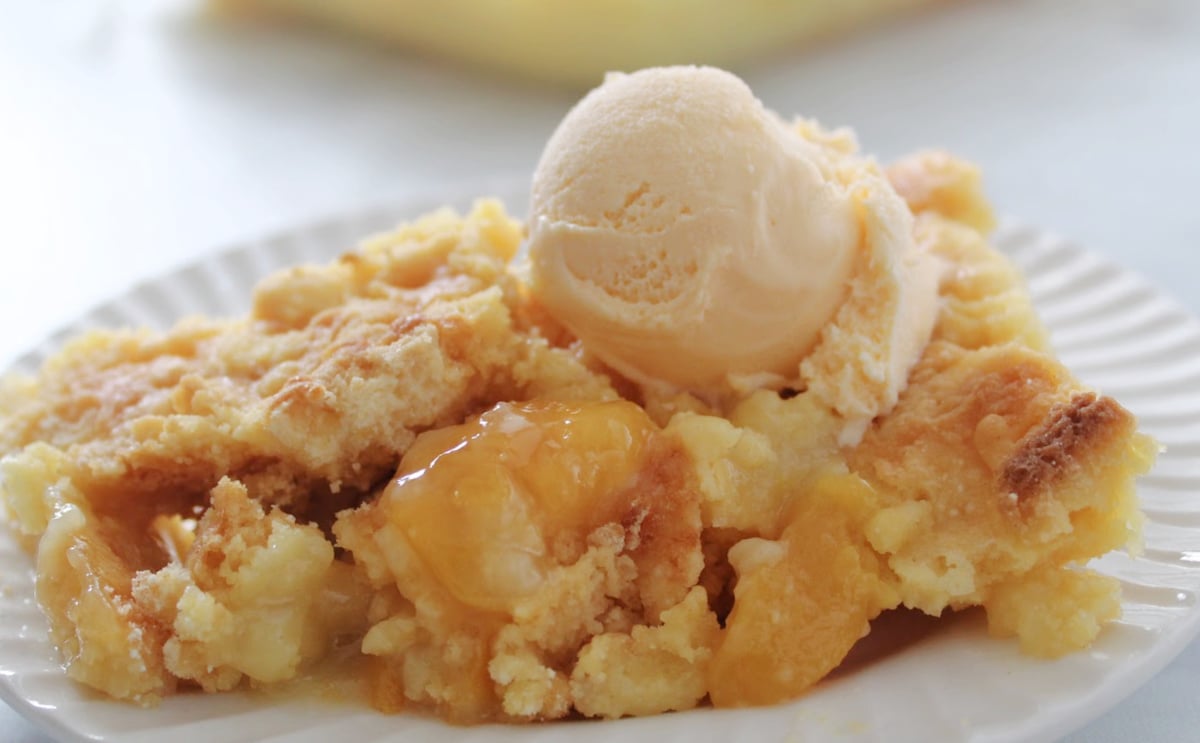 cake mix peach cobbler serving on a white plate with a scoop of vanilla ice cream.