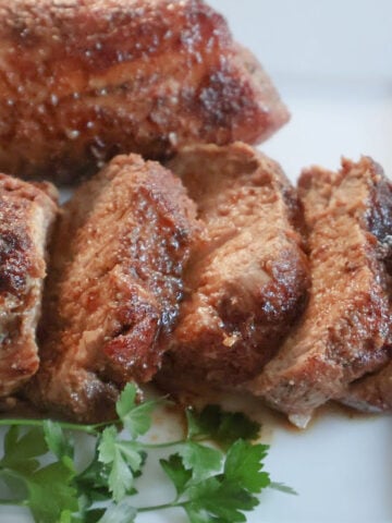 Sliced oven roasted tenderloin. It has a sugar caramelized crust and the pork slices are moist and tender .