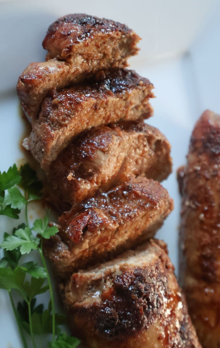 roasted juicy pork tenderloin on a tray. Slices are moist and juicy with a carameled crust.