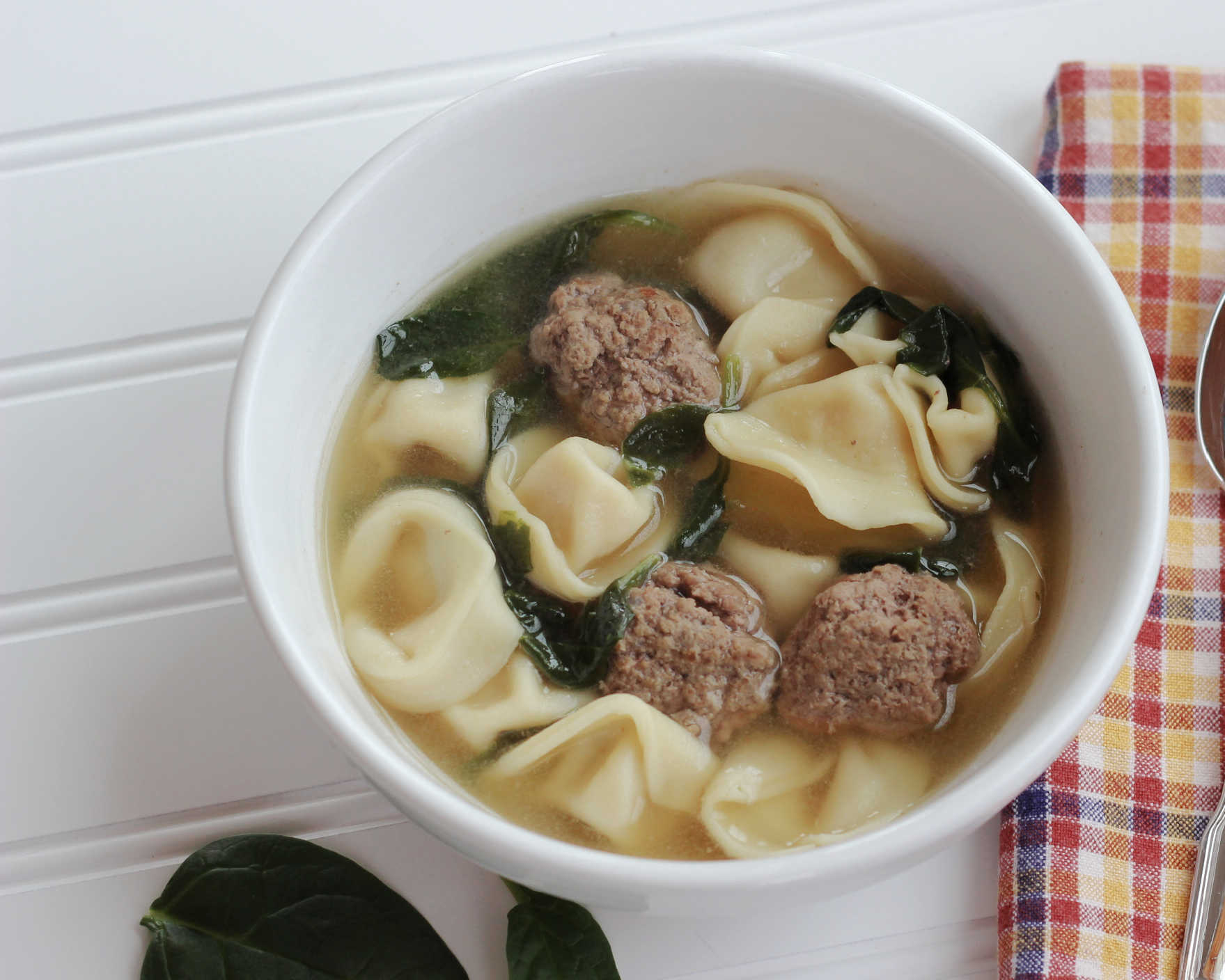 tortelini meatball soup with spinach. Served in a white bowl.