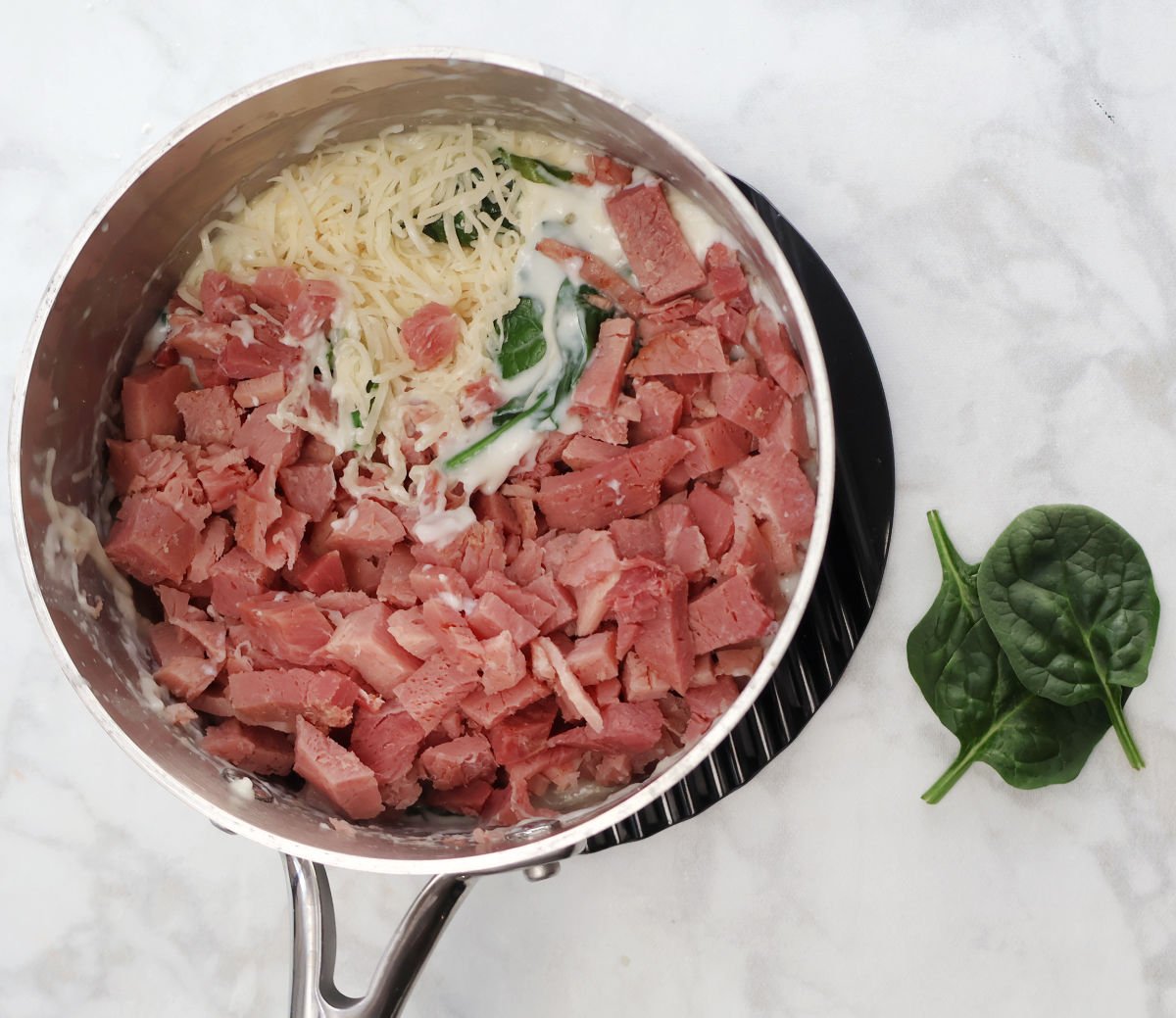 adding ham and swiss cheese to the sauce with fresh spinach.