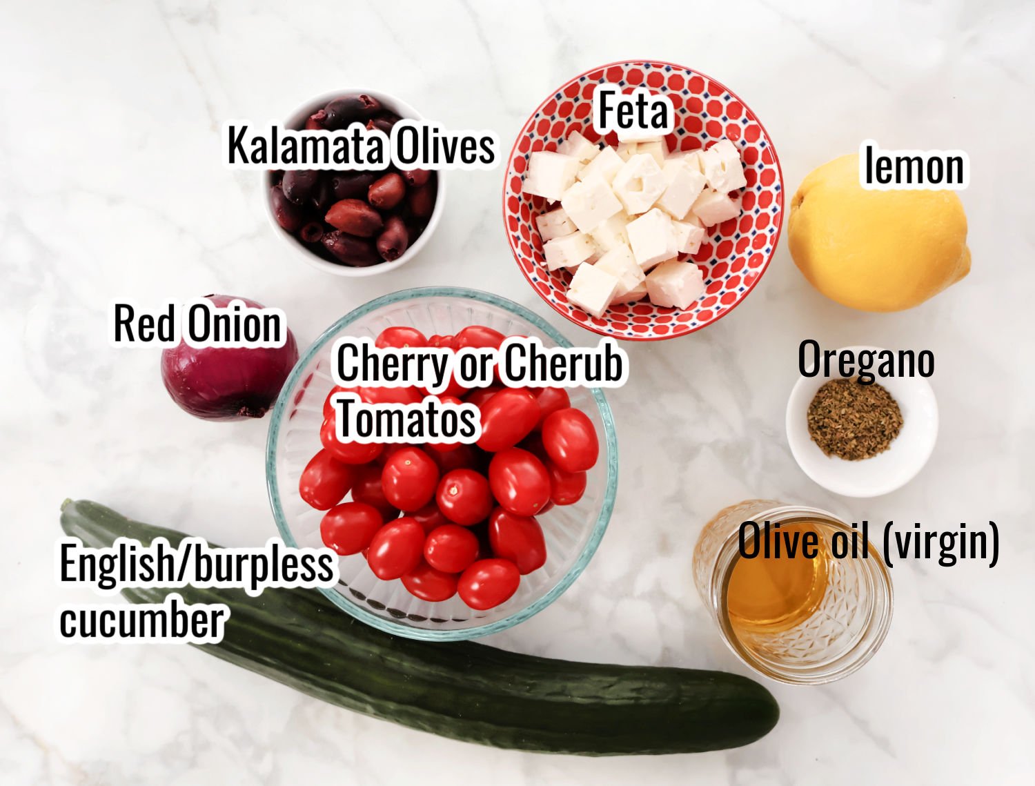 Ingredients for this greek style salad including cherry tomatoes, English cucumber, red tomato, kalamata olives, feta, olive oil, oregano, lemon.